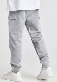 Grå fleece cargo bukser med sidelommer, indsnævret ankellukninger og en blød tekstur. Sættet er kombineret med hvide sneakers for kontrast.