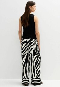 Haut sans manches noir associé à un pantalon large à rayures zébrées noir et blanc, avec un tissu texturé et des accents de rayures horizontales au niveau de l'ourlet.
