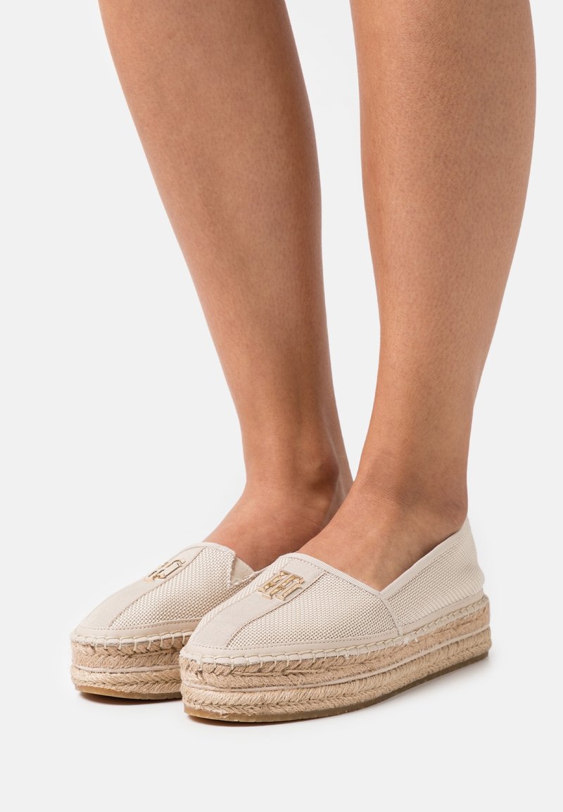 Baskets espadrilles beige avec semelles en jute tissé, tige en tissu texturé et un petit logo brodé à l'avant. Design plat, à enfiler.