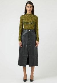 Zielona koronkowa bluzka z długim rękawem ozdobiona kwiatowym wzorem; czarna skórzana spódnica o długości do połowy uda z rozcięciem z przodu i wysokim stanem, zestawiona z czarnymi szpilkami.