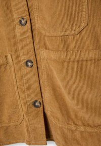 Tessuto in corduroy marrone con strisce verticali prominenti, caratterizzato da bottoni scuri, una tasca sul petto e una superficie testurizzata.