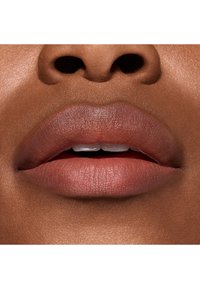 Gros plan sur des lèvres avec une finition mate rose nude ; texture lisse avec un éclat subtil ; forme naturelle, mise en valeur par un teint chaud.