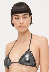 Melna metāla bikini augšdaļa ar trīsstūrveida kausiem, rotāta ar ziedveida pērlēm gar malām. Regulējami kakla un muguras saites.