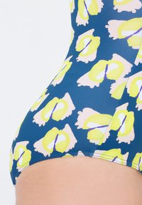 Bañador multicolor con una base azul y grandes patrones florales en amarillo y rosa. Textura suave con una construcción sin costuras.