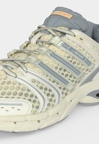 Ανοιχτό μπεζ και γκρι αθλητικό παπούτσι Adidas adiSTAR με διχτυωτό επάνω μέρος, γκρι κορδόνια και μαλακή σόλα, εμφανίζοντας λεπτομέρειες πλάγια και πάνω.