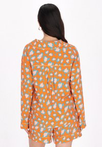 Orange pyjamaset med leopardmönster i rosa och blått. Långärmad, kragad topp och shorts med uppvikta ärmar. Slät textur.