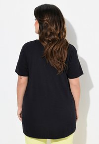 Sort kortærmet t-shirt med en buet kant, lavet af et blødt stof. Bagsiden har en afslappet pasform og en rund halsudskæring.