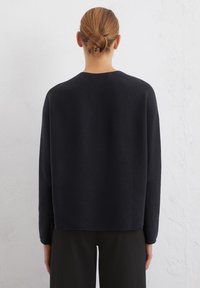 Schwarzer Pullover mit lockerer Passform, Rundhalsausschnitt und langen Ärmeln. Weicher Stoff und minimale Nähte, kombiniert mit dunklen Hosen.