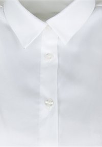 Camicia bianca con colletto classico, texture liscia e bottoni perlacei lungo la parte frontale. Nessun motivo o accento visibile.