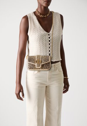 Gilet en tricot beige avec un décolleté en V profond et des détails de boutons, associé à un pantalon large beige clair. Le sac présente une chaîne dorée et un imprimé léopard texturé.