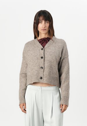 Cropped, light brown cardigan made of soft material, featuring a V-neck, button closure, and ribbed cuffs, paired with light trousers.
