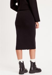 Jupe midi noire avec une silhouette ajustée, texture douce et une fente sur le côté, associée à des bottines noires chunky et des chaussettes blanches.