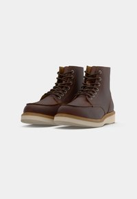 Bottes en cuir marron à lacets avec des semelles en caoutchouc beige, conçues pour une utilisation décontractée ou en extérieur, présentées côte à côte sur un fond gris.