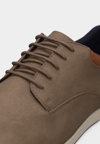 Καφέ σουέτ δετό παπούτσι με στρογγυλή μύτη, ελάχιστα ράμματα και λευκή σόλα, φωτογραφημένο από κοντινή γωνία.