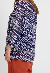 Luftig, gennemsigtig bluse i navy med et hvidt zigzag-mønster. Har trekvartærmer og en rund kant, tekstureret stof.