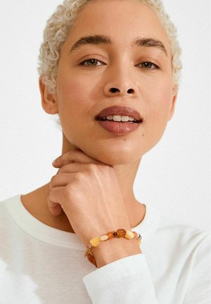 Perlenarmband mit einer Mischung aus abgerundeten, polierten Steinen in Amber-, Gelb- und Brauntönen, mit einem flexiblen elastischen Band.