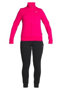 Tenue de sport féminine avec une veste zippée rose vif et un pantalon noir ajusté, les deux arborant le logo Puma sur le côté gauche supérieur.