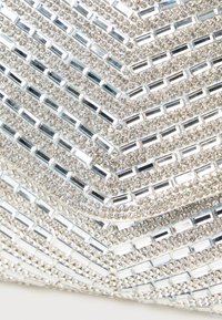 Model Chevron format din mici strasuri transparente și oglinzi dreptunghiulare argintii care formează o suprafață strălucitoare și texturată.