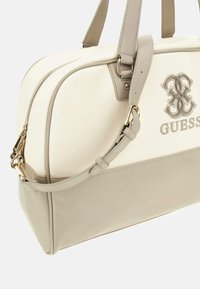 Borsa a spalla in tela beige con dettagli in finta pelle grigia liscia, doppi manici, chiusura con zip e logo "GUESS" impresso. Dettagli in hardware dorato.