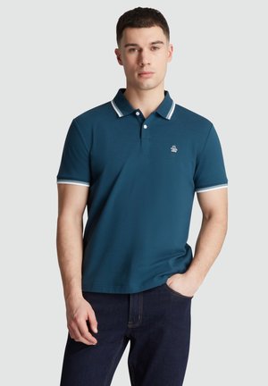 Donkerblauwe polo met witte accenten op de kraag en mouwen, met een klein geborduurd logo op de borst. Gladde katoenen stof.