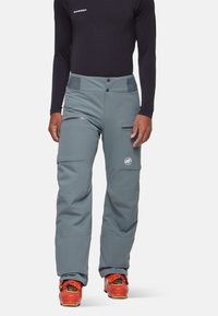 Pantalons de ski gris en matériau résistant, dotés de deux poches avant, d'un patch logo et d'un ajustement réglable. Portés avec des chaussures de ski orange vif.