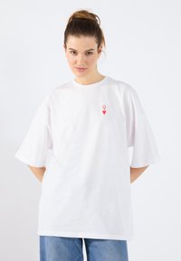 Balta per didelį t-shirt'ą pagaminta iš medvilnės, su mažu raudonu širdies ir rašto grafiku kairėje krūtinės pusėje. Trumpomis rankovėmis ir apvaliu kaklu.