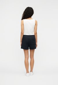 Shorts bleu marine en tissu doux, dotés d'une ceinture élastique et d'une poche arrière. Portés avec un haut sans manches blanc et des baskets blanches.