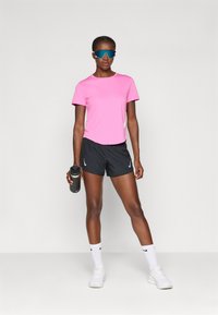 Rosa kortermet treningsskjorte, sorte shorts, hvite sokker og hvite joggesko. Holder en svart vannflaske, har på seg blåtonede solbriller.
