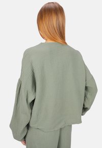 Grüner, texturierter, übergroßer Pullover mit lockerer Passform, tiefen Schultern und einem Saum, der an den Seiten leicht nach oben gebogen ist.