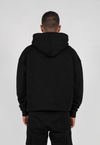 Svart hettegenser laget av myk stoff; har en avslappet passform og ribbede mansjetter. Bakken viser en glatt tekstur og enkelt design.