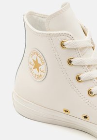 Witte hoge sneakers van leer, met gouden veterogen, een rubberen zool en een ronde logo patch met een ster.