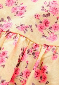 Tela floral con un fondo amarillo claro, con rosas rosas y hojas verdes. El material tiene un acabado suave y ligeramente texturizado con detalles fruncidos.