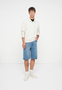 Cămașă polo cu mânecă lungă, crem, pantaloni scurți din denim albastru, pantofi slip-on albi. Design simplu; pantaloni scurți au o croială dreaptă și margine brută.