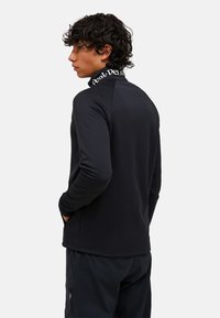 Top nero a maniche lunghe realizzato in tessuto elasticizzato. Presenta un colletto alto con logo a contrasto e un design senza cuciture per un aspetto pulito.