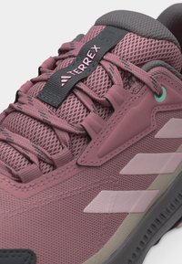 Κοντινό πλάνο μοβ αθλητικού παπουτσιού Adidas Terrex που δείχνει το ύφασμα από δίχτυ, τα κορδόνια και το λογότυπο στην γλώσσα του παπουτσιού.