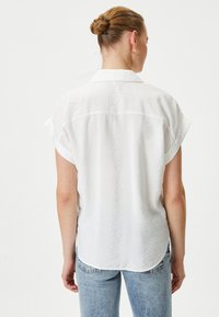 Witte korte mouwen overhemd met een gestructureerde oppervlakte, een rugpand en een afgeronde zoom, gecombineerd met lichte denim jeans.