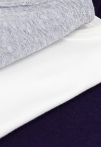 Tre foldede t-shirts i grå, hvid og navy. Den grå skjorte har en meleret tekstur, mens de hvide og navy skjorter er ensfarvede og glatte.