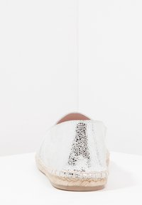 Silver espadrille with metallic sheen, woven jute sole, and textured upper featuring a subtle patterned finish. Rounded back design.