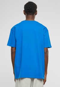 Bl�å bomulds T-shirt, korte ærmer, rund hals, afslappet pasform, glat tekstur, med en lige kant, båret over lyse grå shorts.