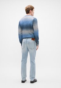 Μπλε γκριάντ μπλούζα πλέξιμου με μακριά μανίκια, συνδυασμένη με ανοιχτό μπλε τζιν και μαύρα παπούτσια. Η μπλούζα διαθέτει στρογγυλή λαιμόκοψη και υφασμάτινη υφή.