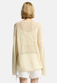 Hellgelbes Strickoberteil mit lockerem, offenem Maschendesign; verfügt über einen weiten Ausschnitt und überschnittene Schultern, mit fransigen Saumdetails.
