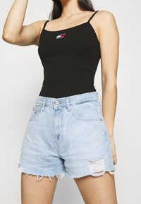 Czarny prążkowany top na ramiączkach z cienkimi paskami z naszywką logo Tommy Jeans, połączony z jasnoniebieskimi szortami dżinsowymi z postrzępionym dołem i przetarciami.