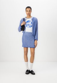 Blue and white patterned knit jacket over a graphic t-shirt and fitted skirt, paired with black loafers and white socks. Contains a black bag.