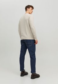 Light beige long-sleeve sweater, fitted style, paired with dark blue denim jeans and black lace-up boots, view from the back.