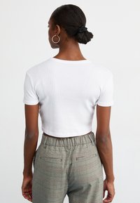 Hvid, kort ribbet t-shirt med korte ærmer, parret med højtaljede ternede bukser med en afslappet pasform og elastisk talje.