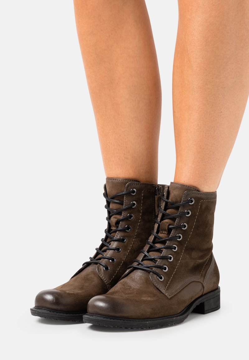 Bottines en daim marron avec lacets noirs, bout arrondi, petit talon carré et surpiqûres décoratives sur le côté et le dessus.