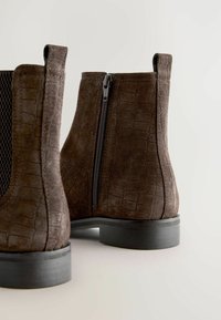 Braune Wildleder-Ankle Boots mit Krokodilmuster, schwarzer elastischer Seitenpartie und schwarzem Reißverschluss; niedriger, stabiler Absatz und abgerundete Zehen.