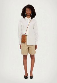 White long-sleeve blouse with a pointed collar, beige shorts, and black flats. A woven tan crossbody bag completes the outfit.