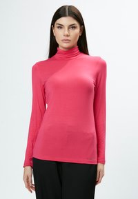 Langärmliges, turtleneck Oberteil in leuchtendem Pink, aus dehnbarem Material mit glatter Textur. Verfügt über ein tailliertes Design und subtile Seitenschlitze.