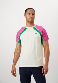 Short-sleeve athletic shirt in cream with pink and green raglan sleeves, featuring textured accents and a small logo on the left chest.